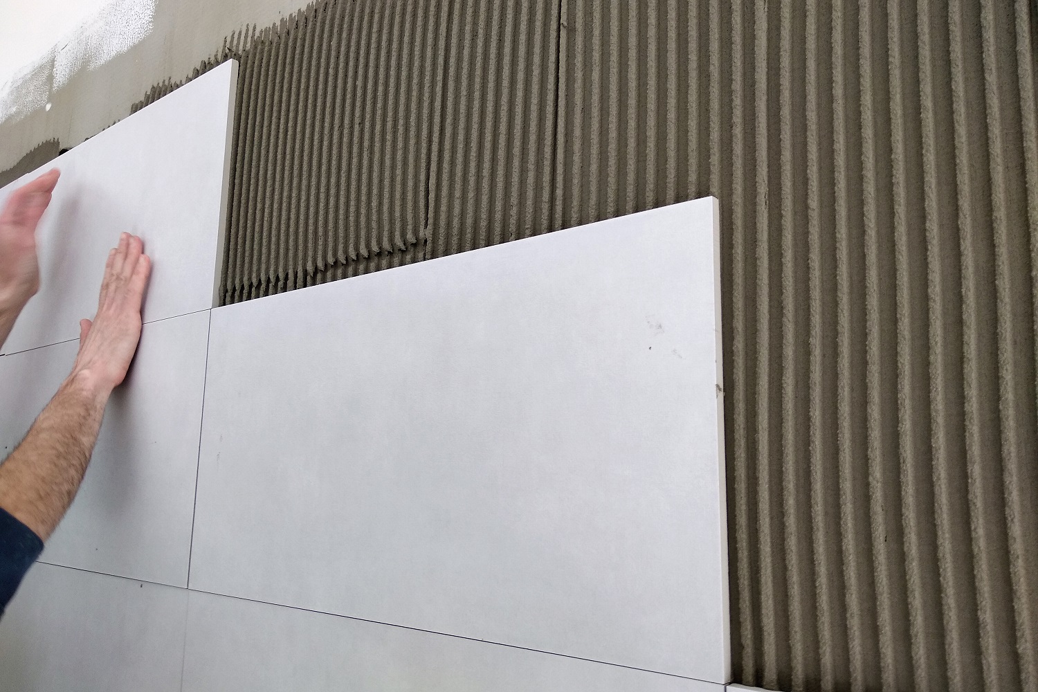 Worker hands putting ceramic tiles on the wall.