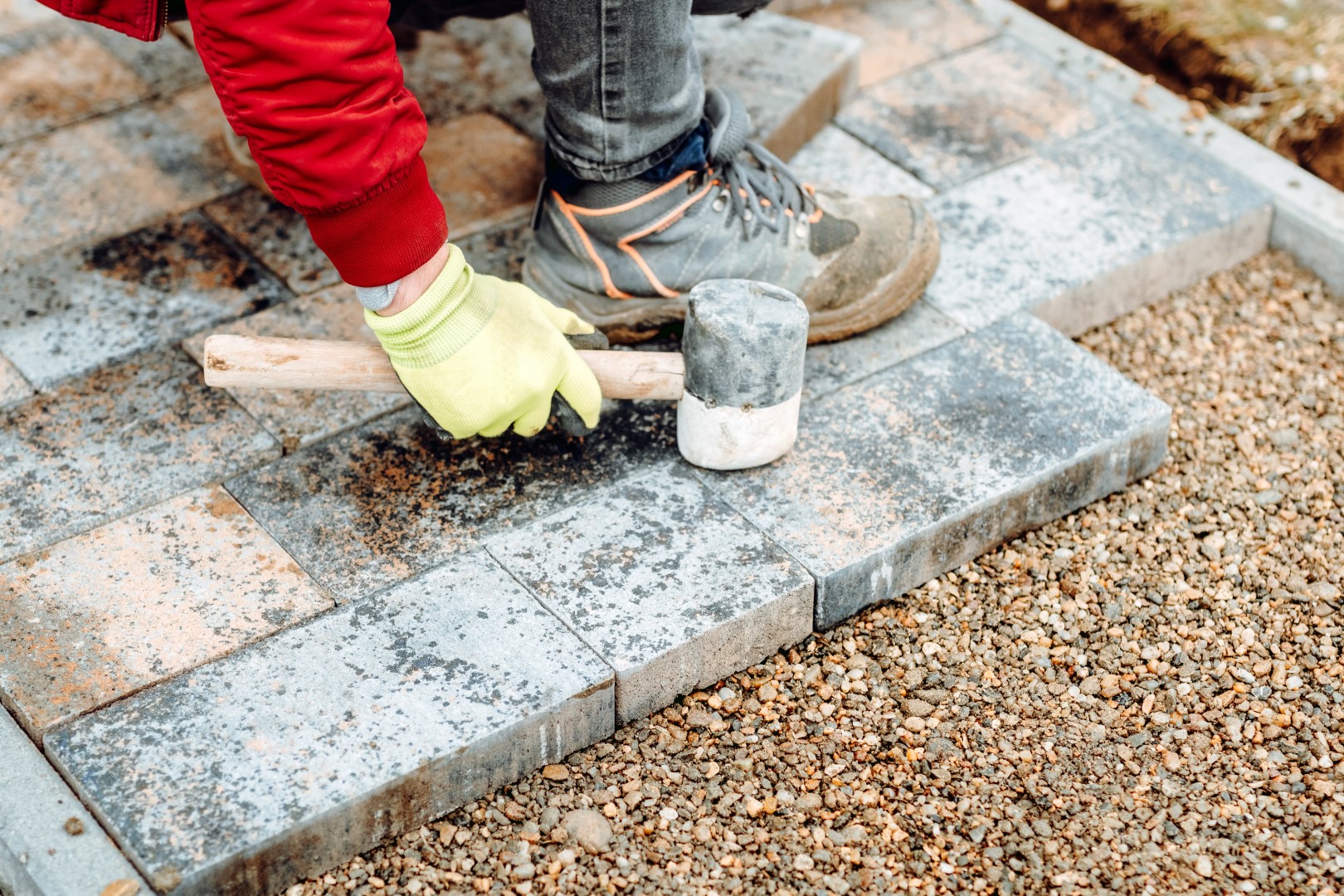 Industrial worker installing concrete paver blocks with rubber hammer and special gloves